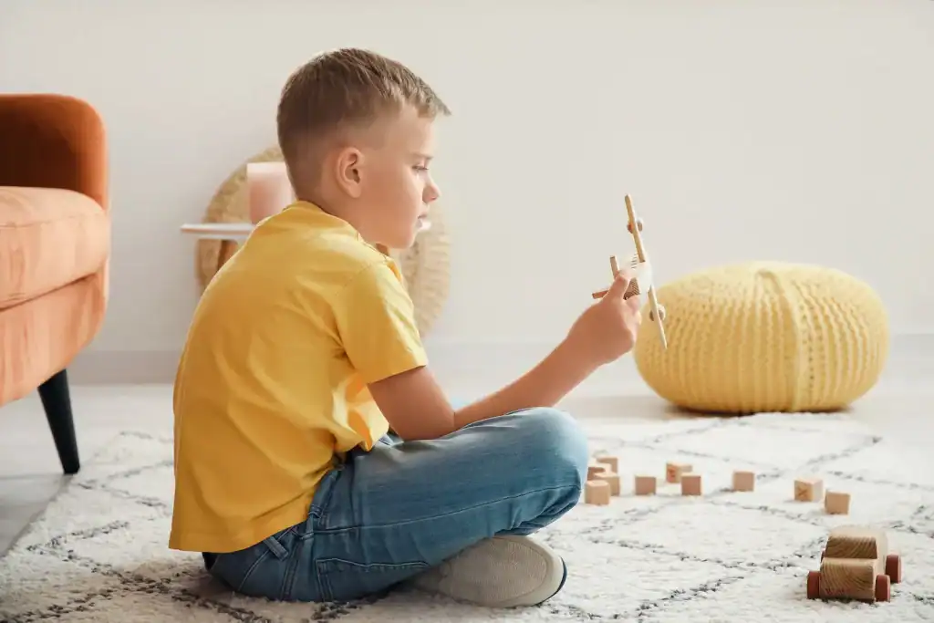 Child engaging in sensory activity with wooden blocks and toy airplane.
