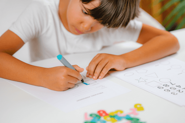 Child completing a dyscalculia assessment worksheet with a pen at a desk.